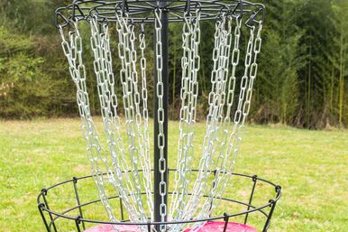 Disc golf basket with metal chains catching a bright pink disc on a grassy park field