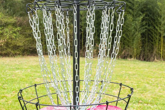 Disc golf basket with metal chains catching a bright pink disc on a grassy park field