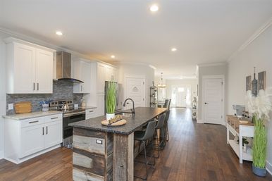 Bright modern farmhouse open-concept kitchen with white cabinets, stainless steel range, large dark granite island with reclaimed wood base and bar stools, hardwood floors and recessed lighting