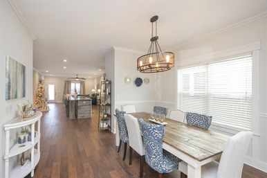 Sunlit modern farmhouse open-plan dining area with reclaimed wood table, blue patterned chairs, industrial chandelier, hardwood floors, kitchen island and a decorated Christmas tree in the distant living area.