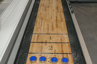 Close-up of an indoor wooden shuffleboard table with numbered scoring zones 1–3 and four blue pucks lined up at the 3-point area
