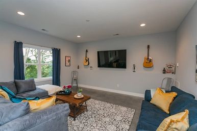 Cozy modern living room with wall-mounted TV, two blue-gray sofas, acoustic guitars on the wall, wooden coffee table and patterned rug