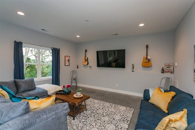 Cozy modern living room with wall-mounted TV, two blue-gray sofas, acoustic guitars on the wall, wooden coffee table and patterned rug