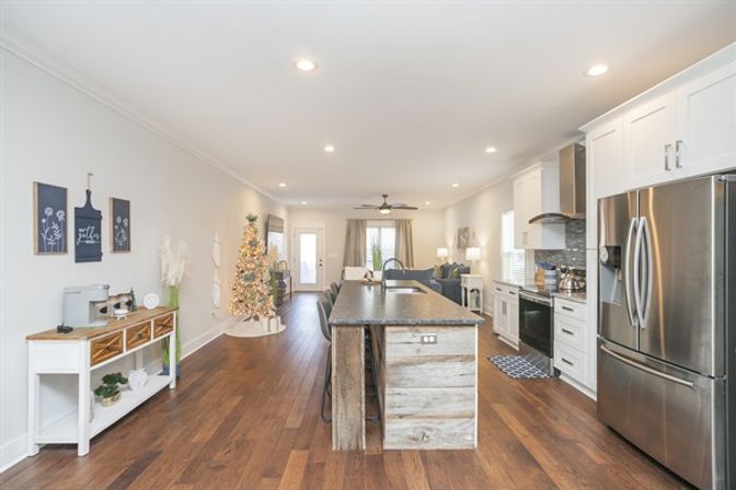 Bright open-concept kitchen and living room with a rustic wood island, stainless steel appliances, white cabinets, warm hardwood floors, and a lit Christmas tree.