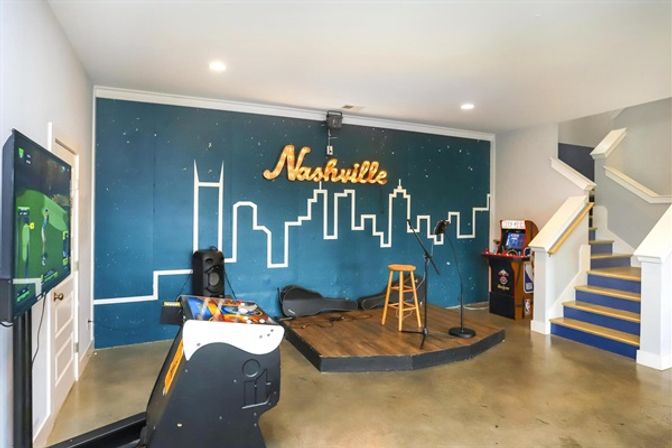 Nashville-themed game and music room with lit skyline mural, small wooden stage with stool and microphones, arcade machine, gaming TV and staircase