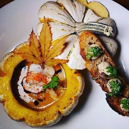 Roasted pattypan squash bowl filled with creamy pumpkin bisque, topped with shrimp, herbs and a maple leaf garnish, served with toasted crostini.