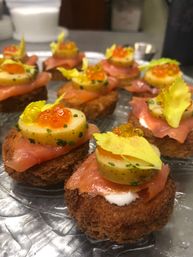 Gourmet smoked salmon canapés on toasted rye rounds topped with sliced baby potato, chives, orange salmon roe and celery leaf — elegant catering appetizer platter