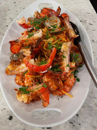 Heaping Italian-style seafood pasta: spaghetti in tomato sauce topped with lobster tail pieces, clams, shrimp and chopped parsley, served on a white oval platter on a marble countertop.