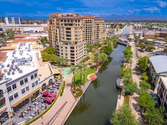 Aerial view of an Arizona urban canal with palm trees, high-rise condos, riverside walkways and outdoor cafés on a sunny day
