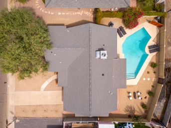 Top-down aerial view of a suburban house with a gray shingled roof, bright turquoise backyard pool, gravel desert landscaping, lounge chairs and patio seating.