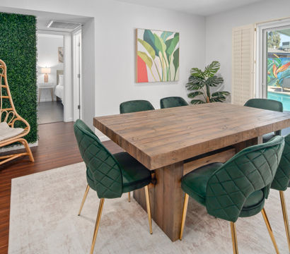 Scottsdale dining area with a chunky reclaimed-wood table, emerald velvet chairs with gold legs, rattan hanging chair by a faux boxwood wall and sliding doors to a pool.