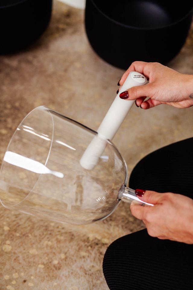 Close-up of hands with red nail polish using a white electric brush to clean a large clear glass vessel on a stone countertop