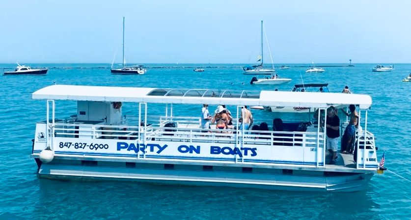 Pontoon party boat with passengers enjoying a sunny summer day on clear blue water, sailboats and motorboats visible on the horizon