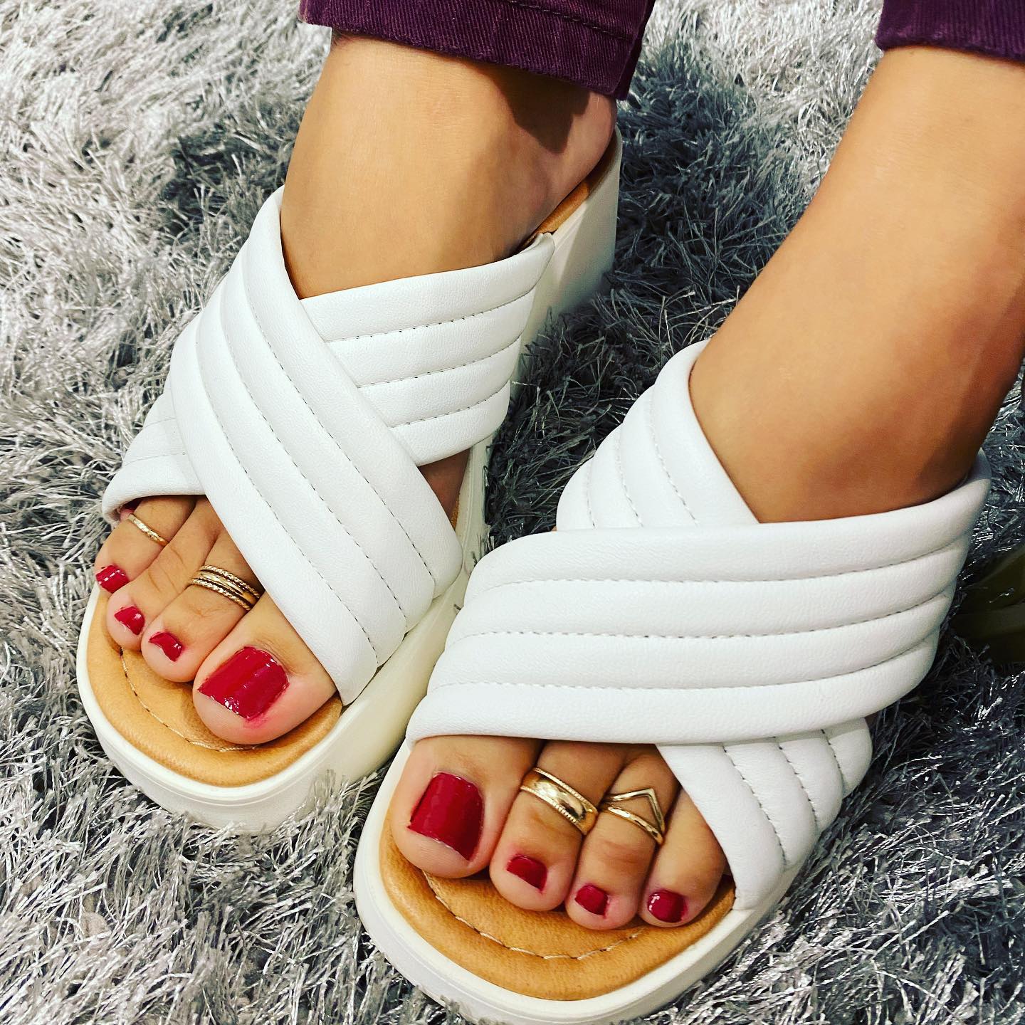 Close-up of feet in white quilted platform sandals with bright red pedicure and gold toe rings on a gray shag rug, stylish women's summer footwear