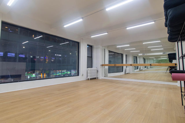 Spacious downtown dance studio with light wood floor, full-length mirrors and ballet barre, large city-view window.