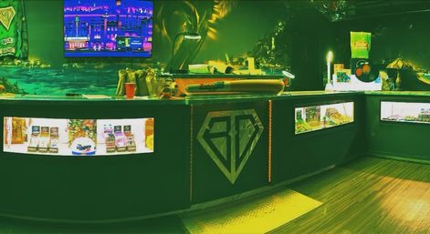 Neon-green lit retail counter with glass display cases of packaged products, a diamond logo on the front, cityscape screen art and warm wood floor in a boutique interior