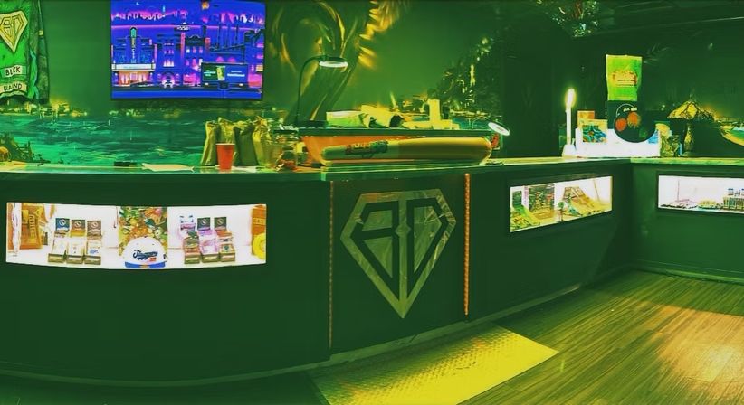 Neon-green lit retail counter with glass display cases of packaged products, a diamond logo on the front, cityscape screen art and warm wood floor in a boutique interior