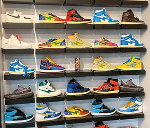 Eye-catching retail sneaker wall display with multiple rows of colorful high-top and low-top streetwear shoes on black floating shelves, featuring bold, pastel and neon designs.