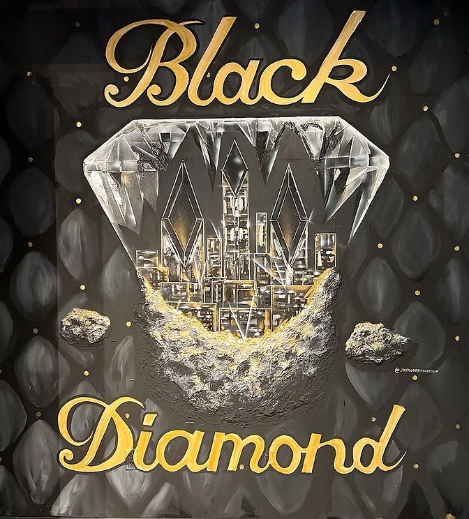 Bold wall mural showing a faceted diamond revealing a gold-lit city skyline and rocky moonlike base on a quilted black backdrop, with gold script reading ‘Black Diamond’.