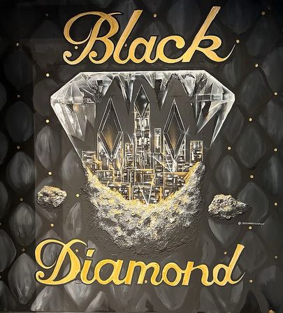 Bold wall mural showing a faceted diamond revealing a gold-lit city skyline and rocky moonlike base on a quilted black backdrop, with gold script reading ‘Black Diamond’.