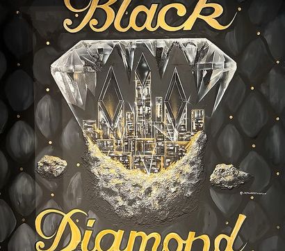 Bold wall mural showing a faceted diamond revealing a gold-lit city skyline and rocky moonlike base on a quilted black backdrop, with gold script reading ‘Black Diamond’.