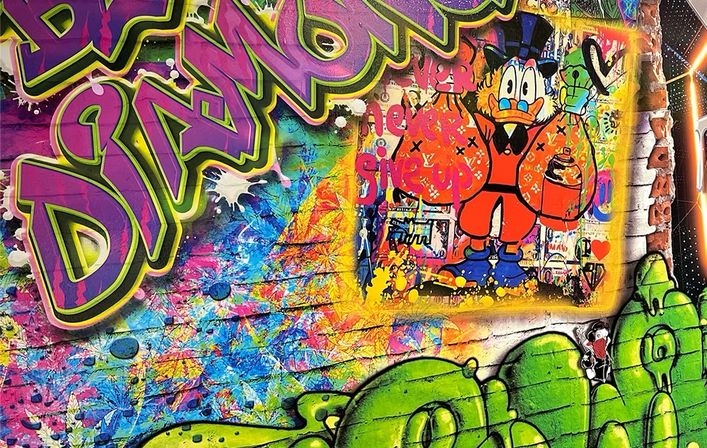 Vibrant street-art mural on a brick wall with layered neon graffiti, splattered paint, bold green bubble letters and a cartoon duck in a top hat holding a spray can.