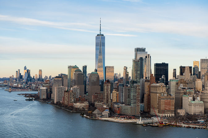 New York City Lower Manhattan skyline with One World Trade Center towering above the Hudson River under a clear evening sky