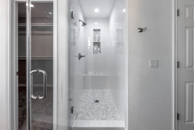 Sleek white walk-in shower with glass door, subway-tile walls, pebble mosaic floor, built-in bench and recessed shampoo niche with chrome fixtures in a modern residential bathroom.