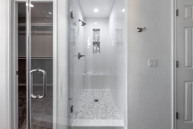 Sleek white walk-in shower with glass door, subway-tile walls, pebble mosaic floor, built-in bench and recessed shampoo niche with chrome fixtures in a modern residential bathroom.