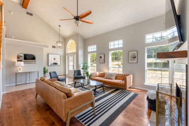 Sunlit modern living room with vaulted ceiling and wooden fan, tan leather sofas, black chairs, striped rug, and tall arched and rectangular windows