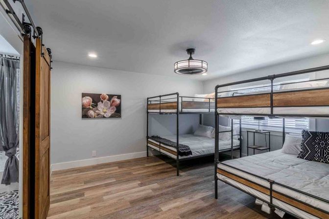Bright modern bedroom with two metal-and-wood double-over-double bunk beds (four beds), sliding barn door, floral wall art, and wood-look floors.