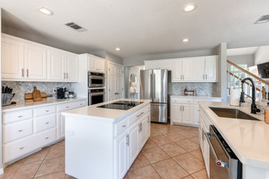 Bright modern white open-concept kitchen with island, quartz counters, stainless French-door refrigerator, built-in ovens, mosaic tile backsplash, and tiled floor.