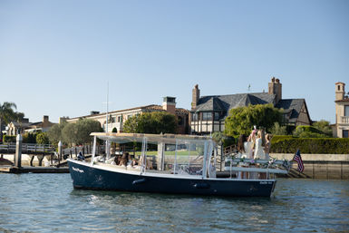 Sunlit leisure boat carrying a group of friends on a bay cruise past grand waterfront mansions and docks at a coastal marina