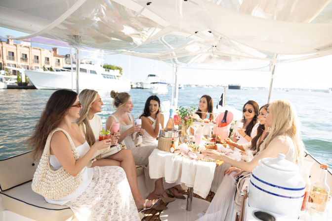 Group of women enjoying a sunny champagne brunch and snacks on a luxury yacht in a coastal marina waterfront.