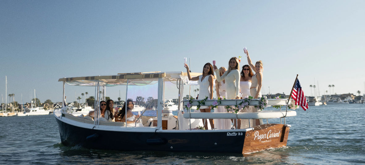 Women in white enjoying a champagne boat party at a sunny marina with an American flag