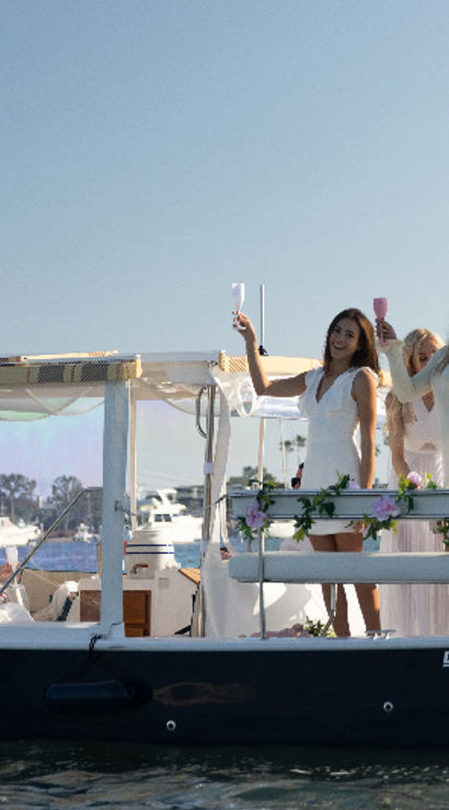 Women in white enjoying a champagne boat party at a sunny marina with an American flag