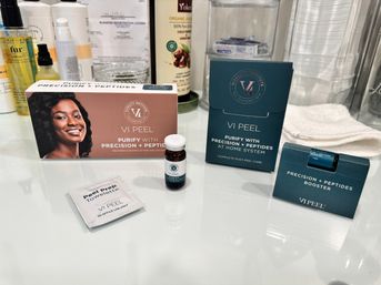 Spa-style bathroom vanity with a chemical peel kit, small serum vials, peel prep towelette and post-peel care boxes arranged on a glossy counter next to towels and skincare bottles.
