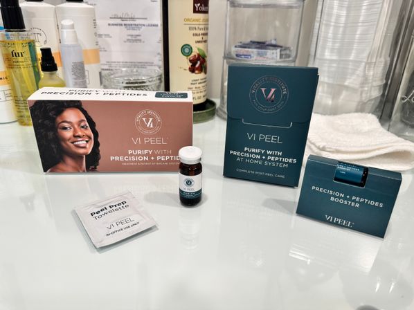 Spa-style bathroom vanity with a chemical peel kit, small serum vials, peel prep towelette and post-peel care boxes arranged on a glossy counter next to towels and skincare bottles.