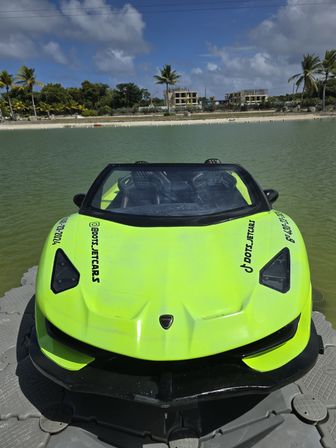 Neon lime-green sport-style jet boat docked on a floating platform in a tropical lagoon with calm turquoise water, sandy beach and palm trees under a partly cloudy blue sky.