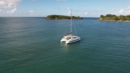 White catamaran anchored in a calm turquoise bay near lush tropical islets under a sunny blue sky