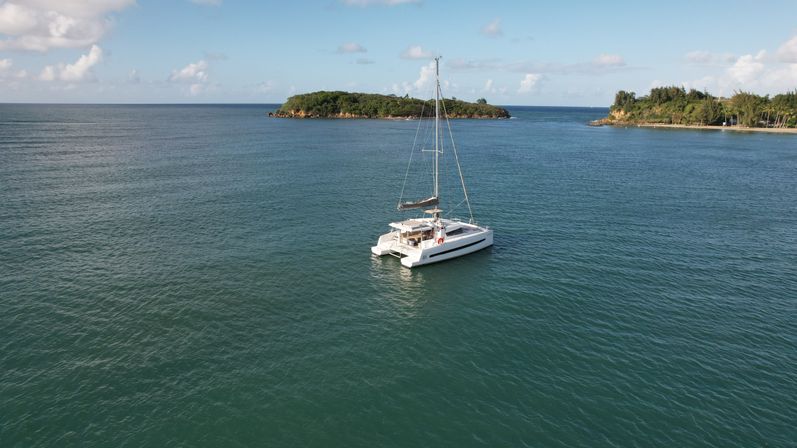 White catamaran anchored in a calm turquoise bay near lush tropical islets under a sunny blue sky