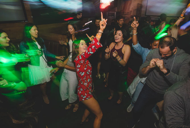 Young adults dancing and laughing on a crowded nightclub dance floor, vibrant green lights and motion blur capturing a lively night out.