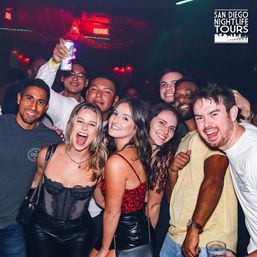 Lively group of friends partying at a San Diego nightclub, smiling and posing under colorful lights with drinks raised.