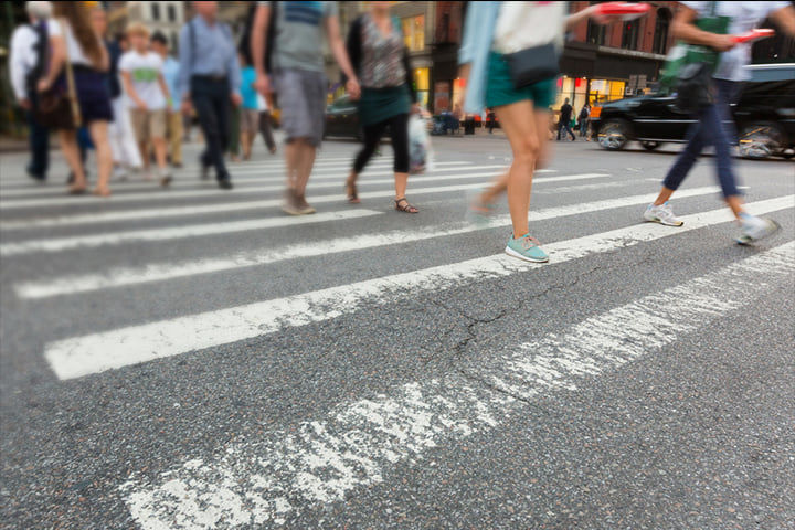 Downtown city crosswalk with blurred pedestrians' legs mid-stride and worn white zebra stripes on asphalt