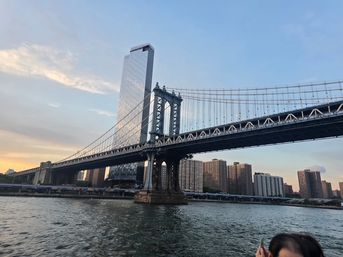 Manhattan Bridge at sunset spanning the East River with a reflective glass tower and New York City skyline of waterfront apartment buildings