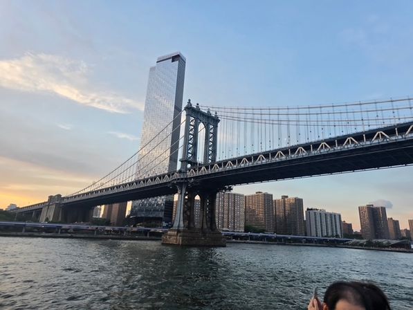 Manhattan Bridge at sunset spanning the East River with a reflective glass tower and New York City skyline of waterfront apartment buildings