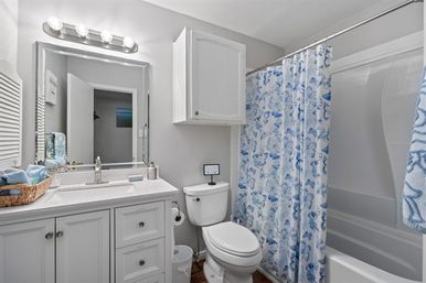 Bright white residential bathroom with modern vanity and lighted mirror, toilet, wall cabinet, chrome fixtures and a cheerful blue floral shower curtain.