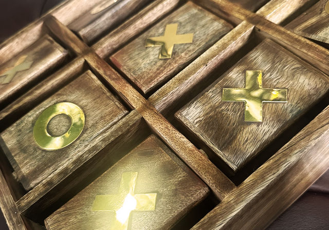 Close-up of a rustic wooden tic-tac-toe board with shiny gold X and O inlaid tiles in a grid
