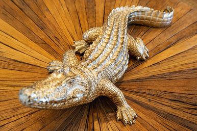 Metallic silver alligator sculpture with detailed scales posed as a decorative centerpiece on a radial wooden sunburst table — close-up home decor accent