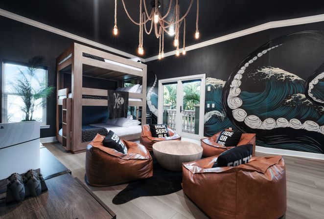 Nautical-themed kids’ lounge with wooden bunk beds, leather bean bag chairs around a round coffee table, dramatic octopus tentacle wall mural, rope pendant lights, and glass doors opening to a balcony with tropical plants — modern coastal bedroom vibe.